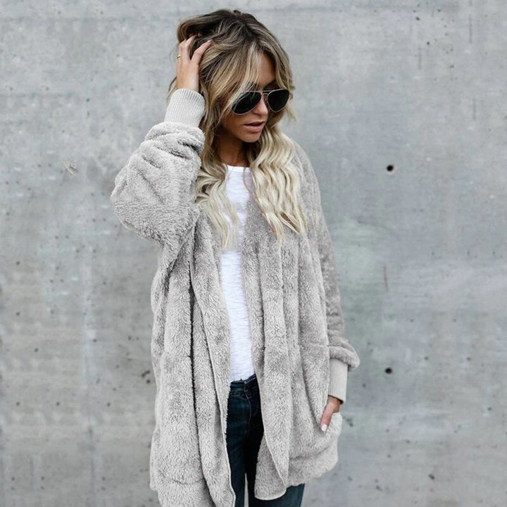 Vrouw in grijze teddyjas, witte trui en zonnebril tegen betonnen muur. Modieuze winterkleding, casual stijl, trendy damesmode.