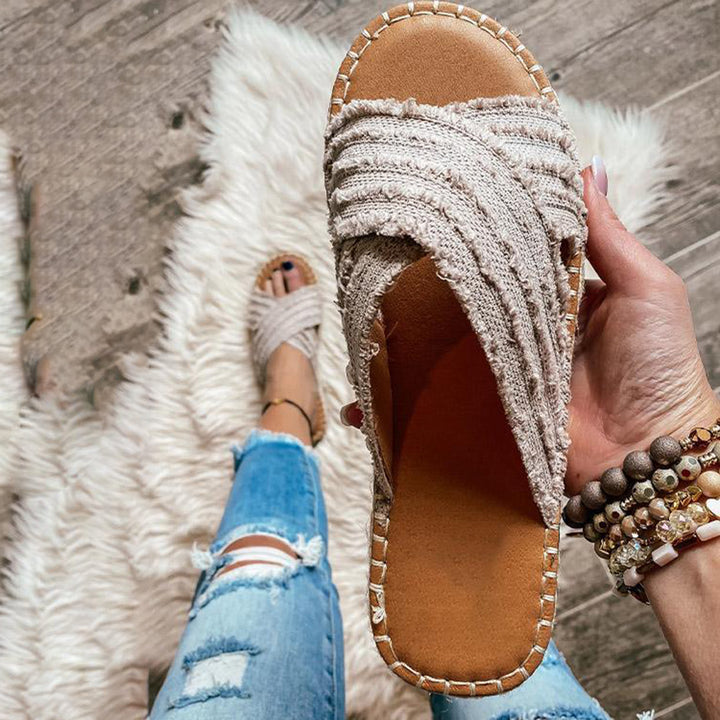 Grijze geweven dames slipper met gevlochten band, comfortabele zool en casual stijl, perfect voor zomerse outfits en strandwandelingen.