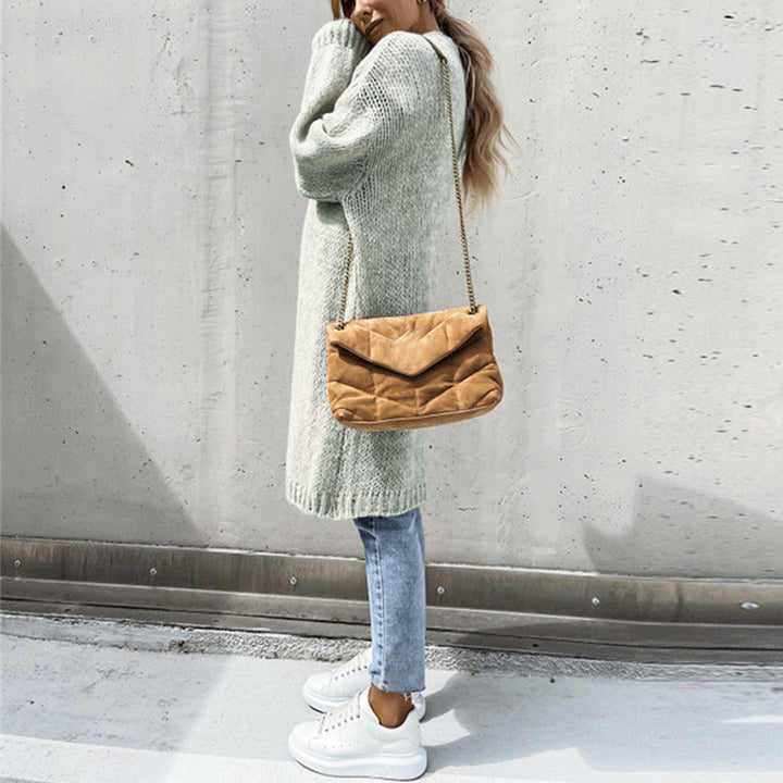 Vrouw in grijze gebreide trui, blauwe jeans en witte sneakers, draagt een bruine schoudertas. Modieuze herfstoutfit, casual streetwear.