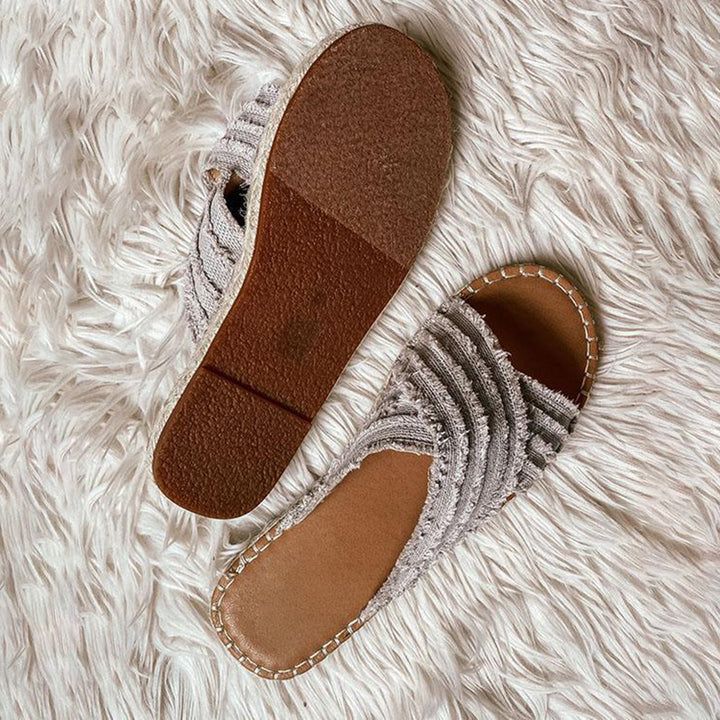 Grijze dames sandalen met franjes op een witte pluizige achtergrond. Comfortabele zomerschoenen, perfect voor casual en strandoutfits.