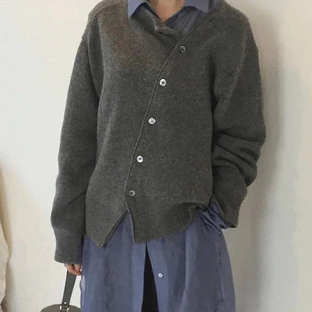 Grijze oversized trui met asymmetrische knoopsluiting, gedragen over een blauwe blouse. Modieuze dameskleding, casual herfst- en winterstijl.