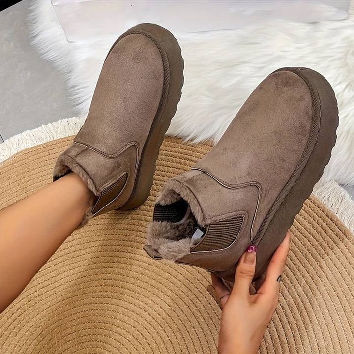 Grijze suède enkellaarsjes met dikke zool en warme voering, gedragen op een beige ronde mat. Perfect voor wintermode en casual outfits.