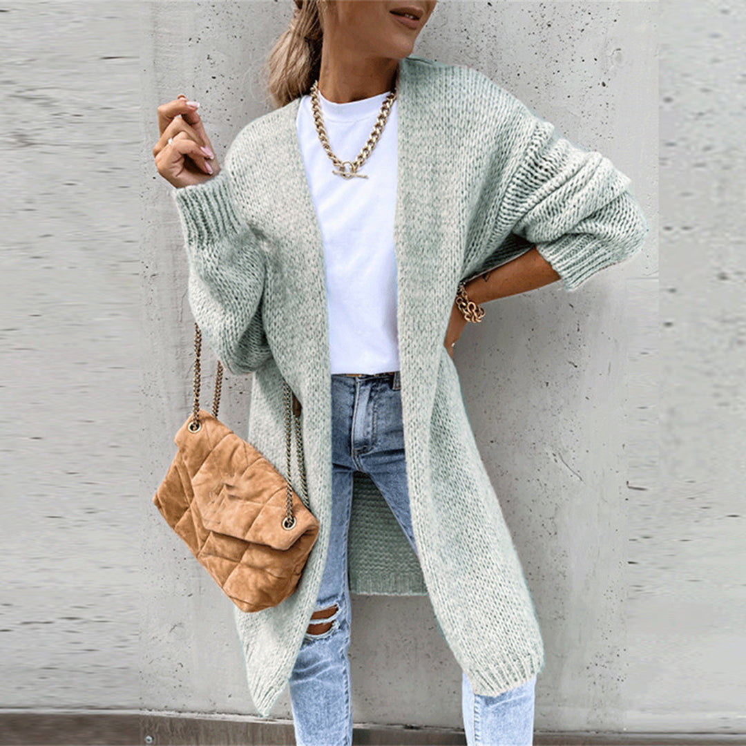 Vrouw in mintgroen gebreid vest, witte top en gescheurde jeans, met bruine schoudertas. Modieuze herfstoutfit, casual dameskleding.