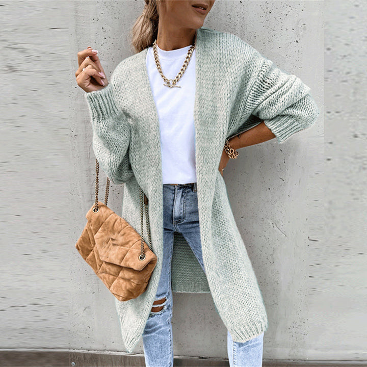 Vrouw in mintgroen gebreid vest, witte top en gescheurde jeans, met bruine schoudertas. Modieuze herfstoutfit, casual dameskleding.