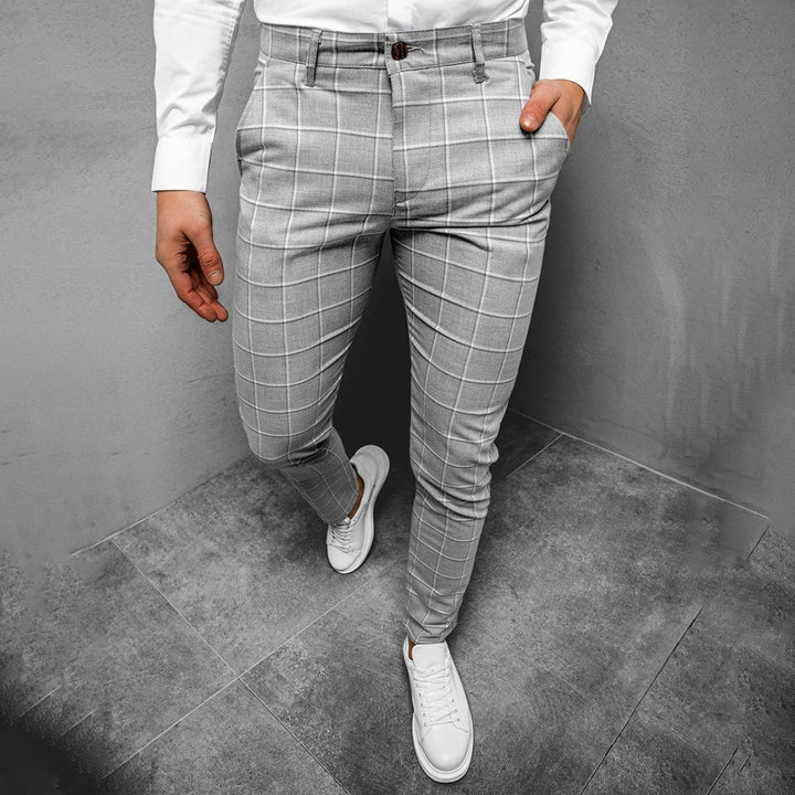Grijze geruite herenbroek, slim fit, gedragen met witte sneakers en een wit overhemd. Stijlvolle casual outfit voor moderne mannen.