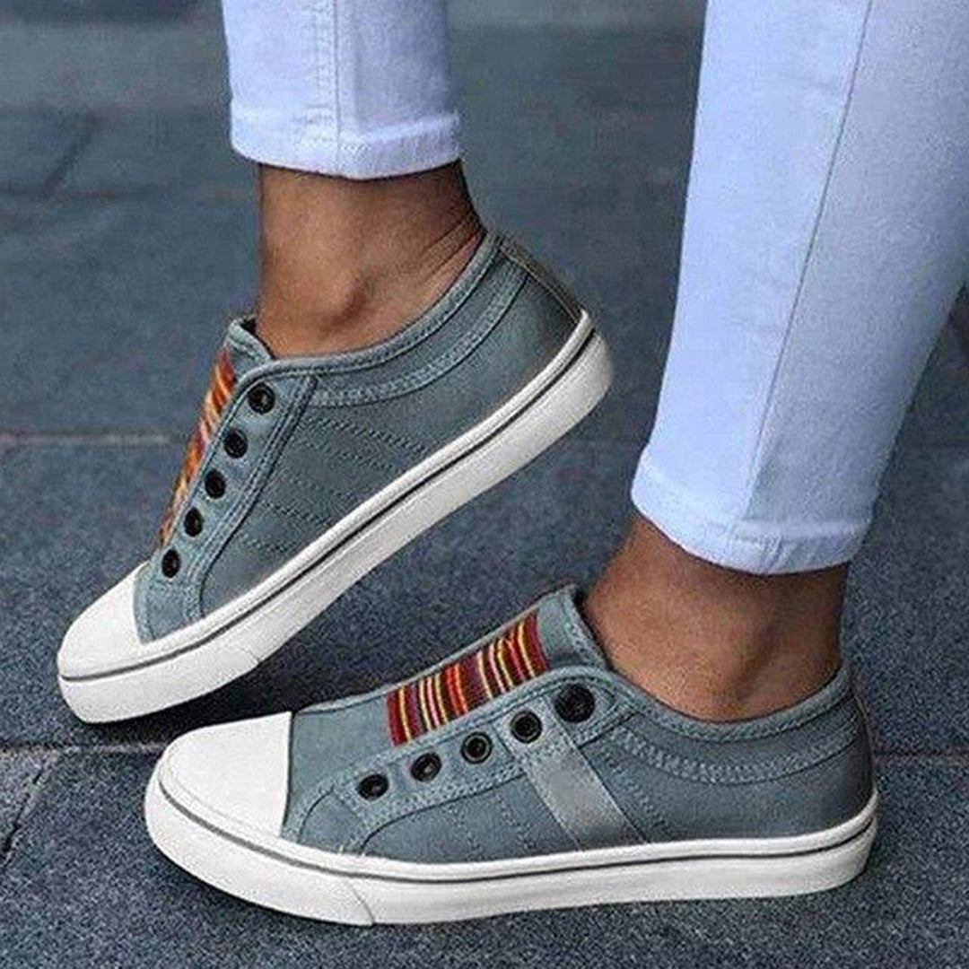 Grijze canvas sneakers met witte zolen en kleurrijke strepen, gedragen door persoon in witte broek. Casual schoenen, unisex mode, comfortabele stijl.