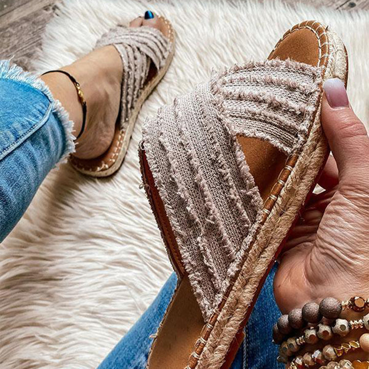 Grijze geweven sandalen met espadrillezool, gedragen door een persoon op een witte vloerkleed. Modieuze zomerschoenen, casual stijl.