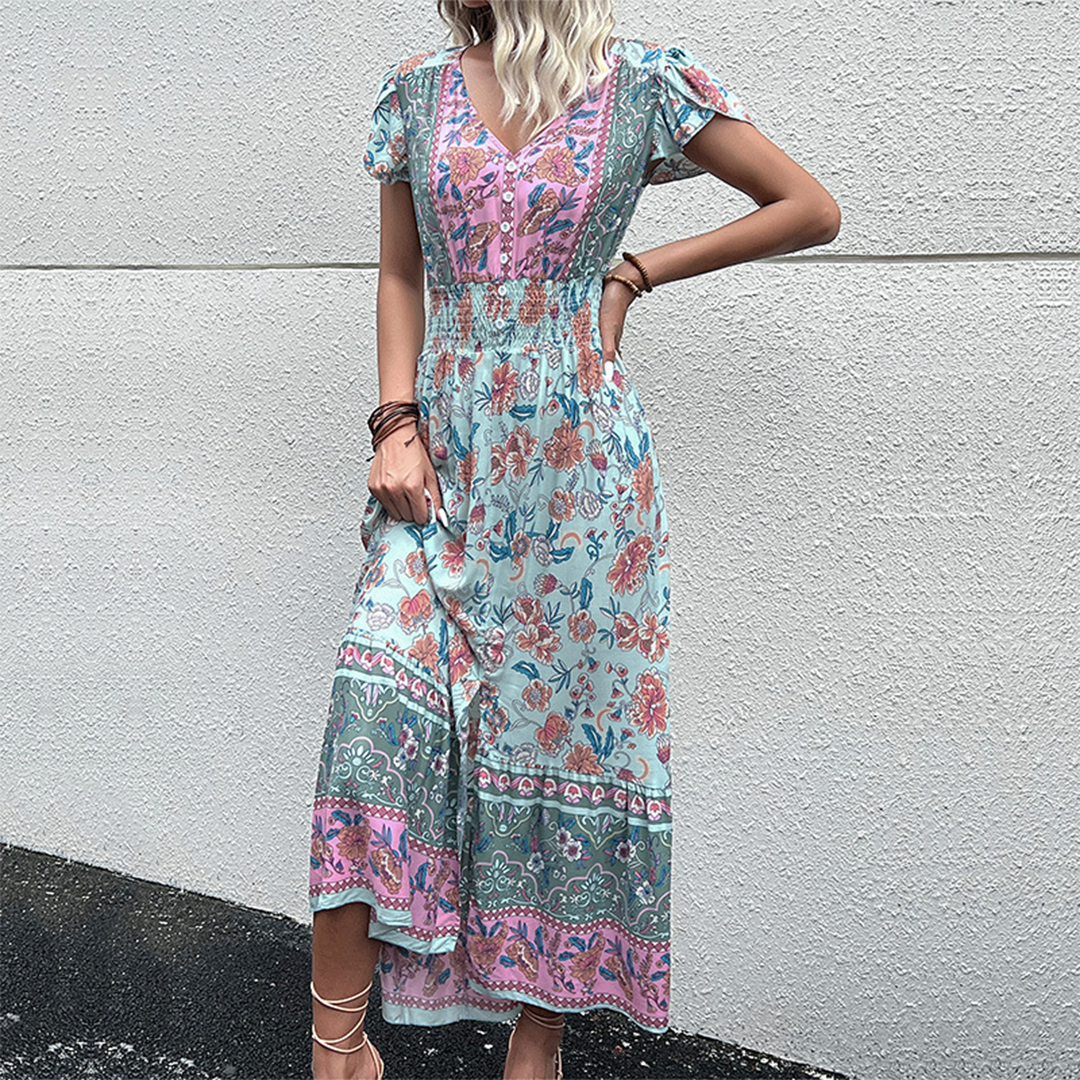Vrouw in lange, kleurrijke boho-jurk met bloemenprint tegen witte muur. Zomermode, bohemian stijl, casual kleding.