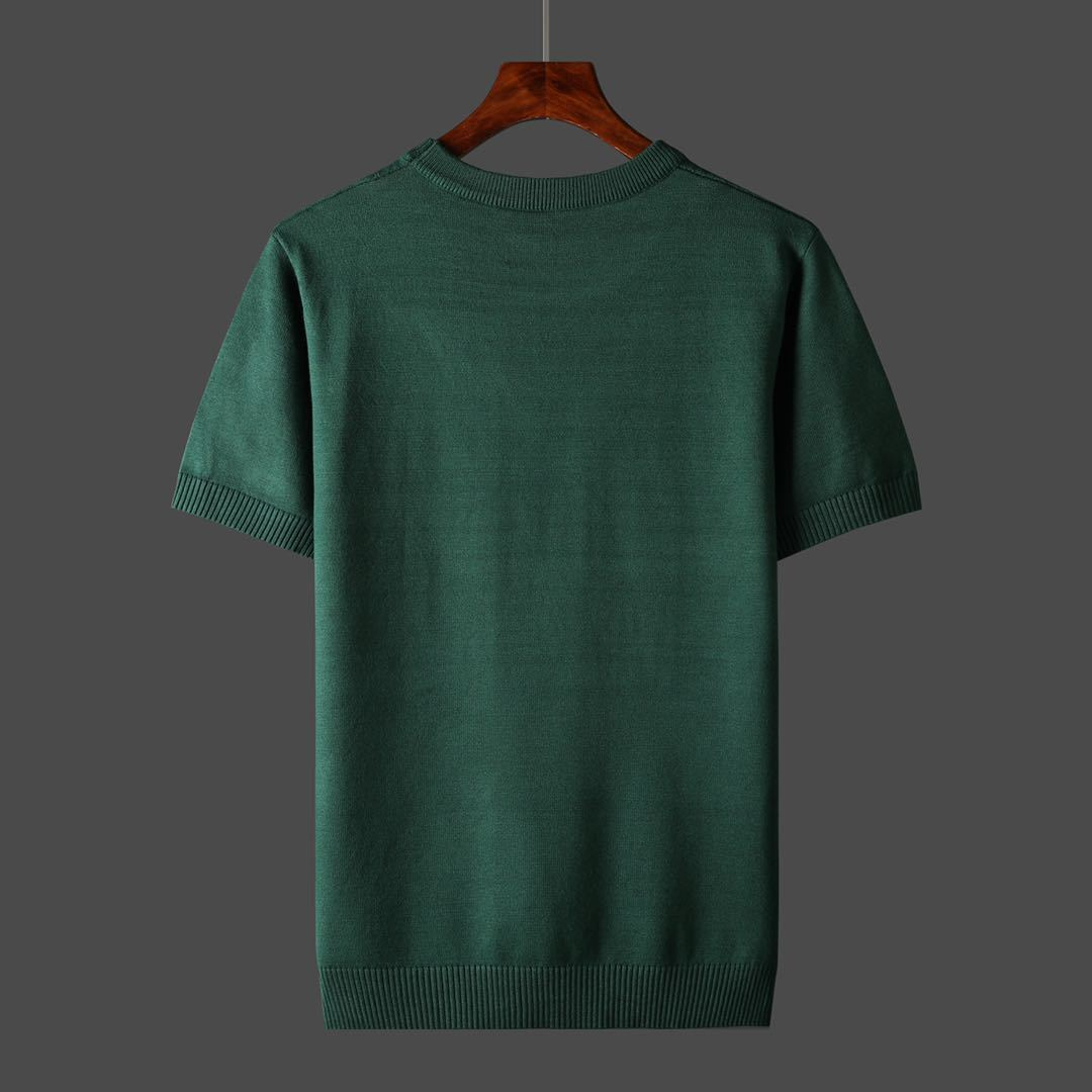 Groene katoenen trui met korte mouwen, minimalistisch ontwerp, op houten hanger tegen grijze achtergrond. Perfect voor casual en stijlvolle outfits.