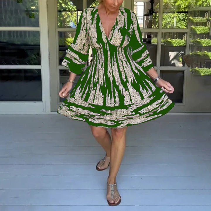 Groene zomerjurk met abstract patroon, gedragen door vrouw op terras. Perfect voor casual en elegante zomerdagen. Comfortabele pasvorm, trendy design.