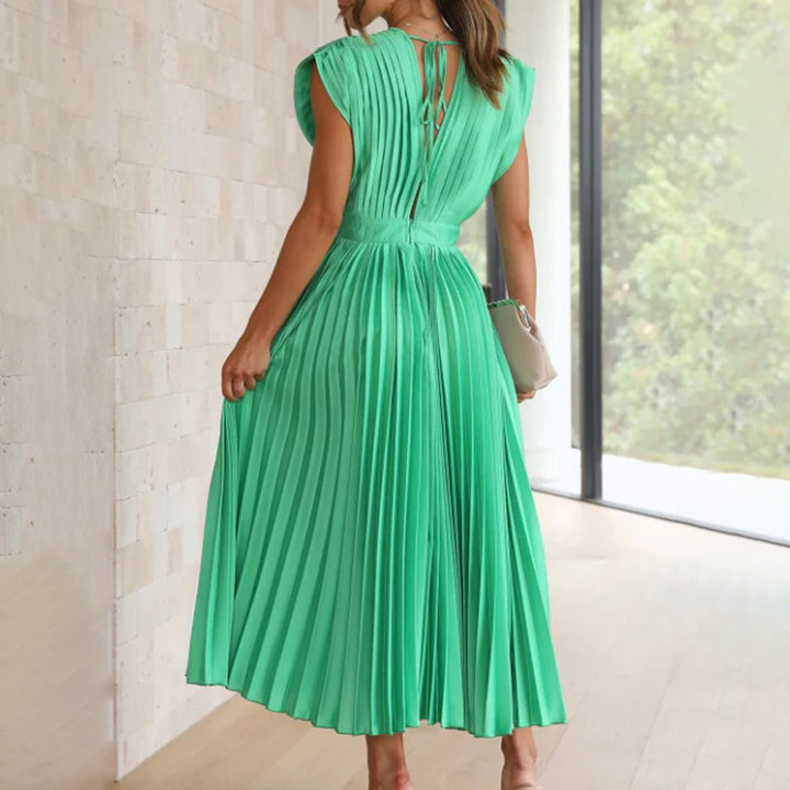Groene geplooide jurk met open rug, gedragen door vrouw in moderne interieursetting. Perfect voor zomer- en avondkleding. Elegante modekeuze.
