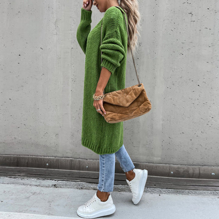 Vrouw in groene oversized trui, blauwe jeans en witte sneakers, draagt een bruine schoudertas. Modieuze herfstoutfit, casual streetstyle.
