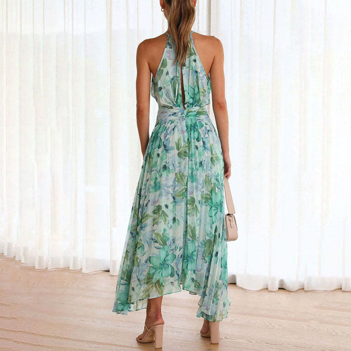 Vrouw in elegante groene bloemenjurk met halternek, staand voor witte gordijnen. Zomerse mode, stijlvolle dameskleding, casual chique look.
