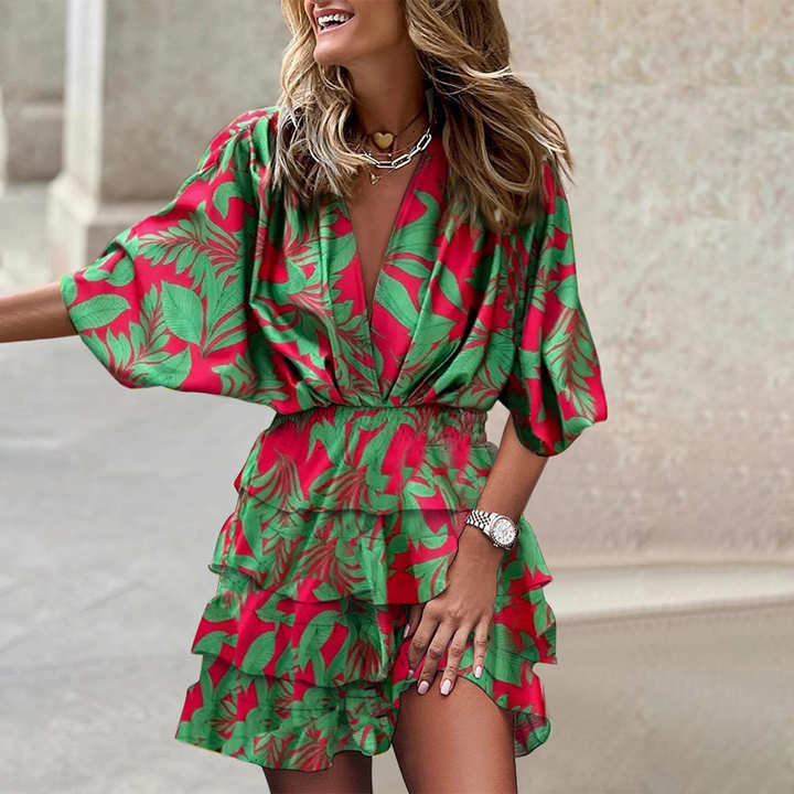 Vrouw in kleurrijke zomerjurk met groene bladeren en rode achtergrond, modieuze outfit, trendy kleding, zomermode, straatstijl.