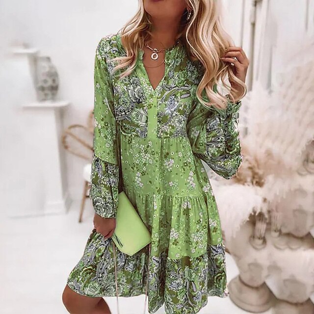 Vrouw in groene bloemenjurk met lange mouwen, holding een groene clutch. Trendy damesmode, lente outfit, casual chique stijl.