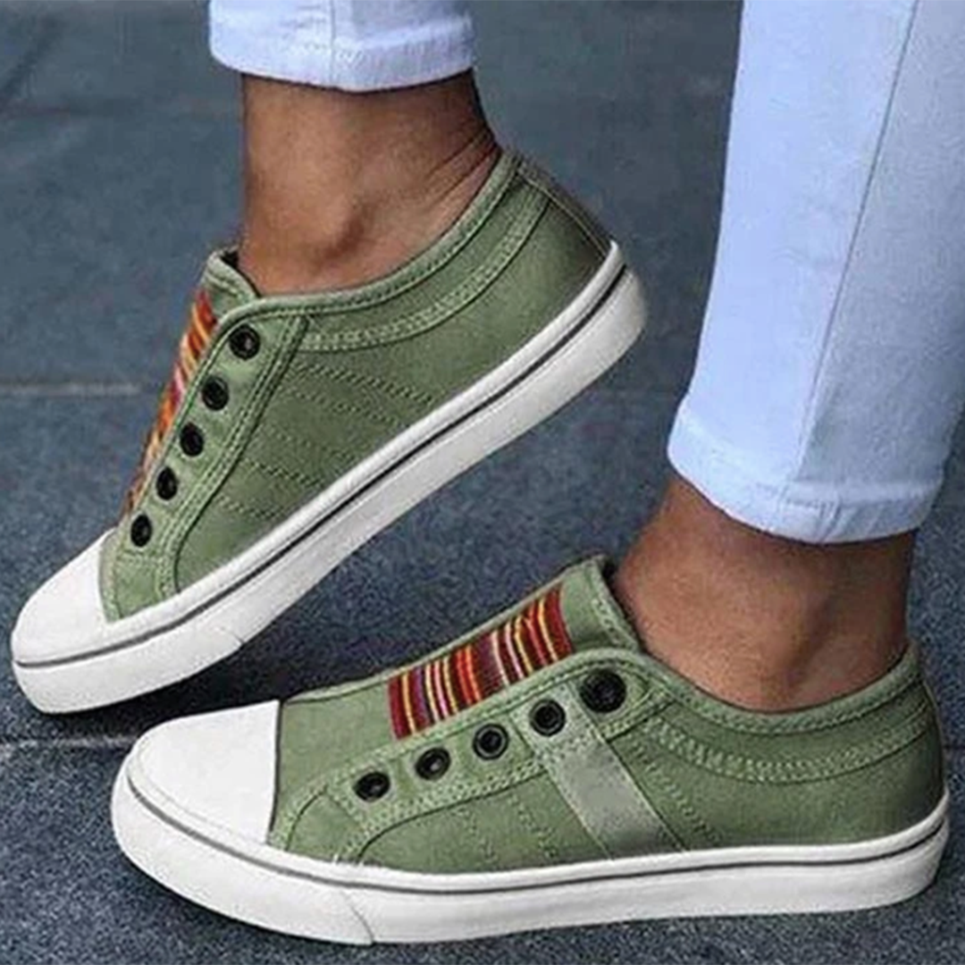 Groene canvas sneakers zonder veters, met kleurrijke strepen en witte zolen, gedragen door persoon in witte broek. Casual en trendy schoenen.