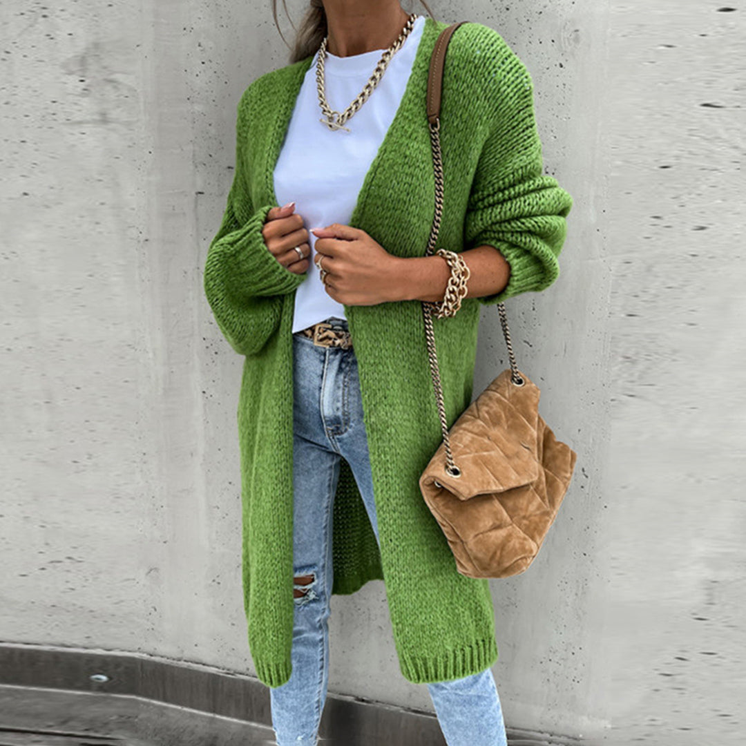 Vrouw in groene gebreide cardigan, witte T-shirt, blauwe jeans, bruine tas. Modieuze herfstoutfit, casual streetwear, trendy dameskleding.