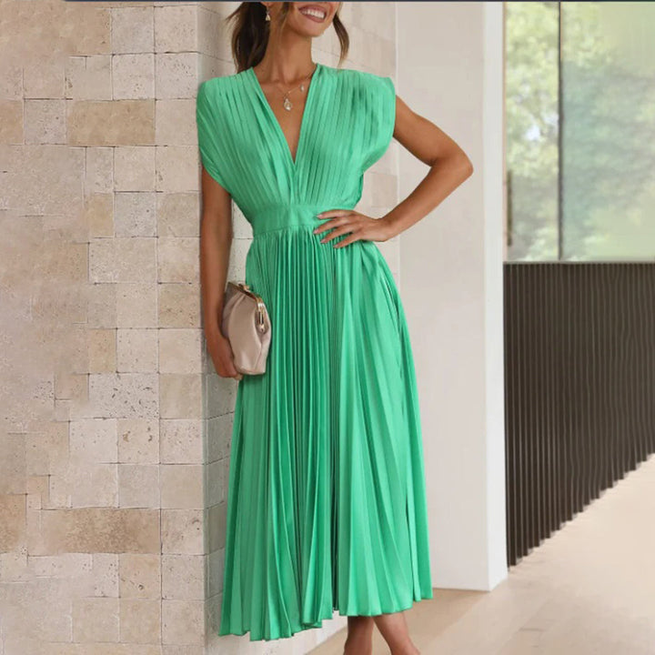 Groene geplooide midi-jurk met V-hals, mouwloos ontwerp en elegante uitstraling, perfect voor zomerse gelegenheden. Accessoires: beige clutch.