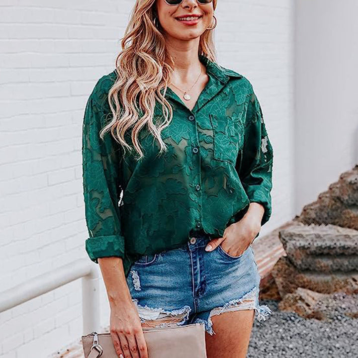 Vrouw in groene blouse met bloemenpatroon, draagt denim shorts en zonnebril, houdt beige clutch. Casual zomeroutfit, modetrend 2023.