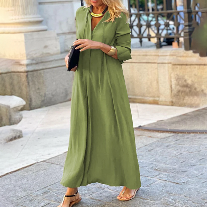 Vrouw in groene maxi-jurk met lange mouwen, gouden ketting en zwarte clutch, wandelend op straat. Stijlvolle zomeroutfit, casual chique mode.