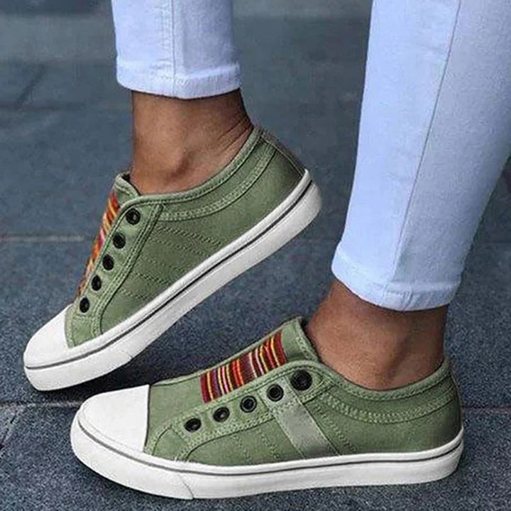 Groene canvas sneakers met kleurrijke strepen, witte rubberen zool en zwarte veterogen, gedragen met witte broek. Casual damesmode schoenen.