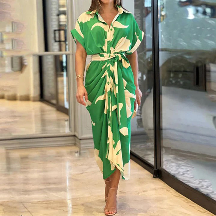 Groene damesjurk met witte print, knoopsluiting en strikceintuur, gedragen in een moderne winkelomgeving. Perfect voor zomerse mode en casual chic.