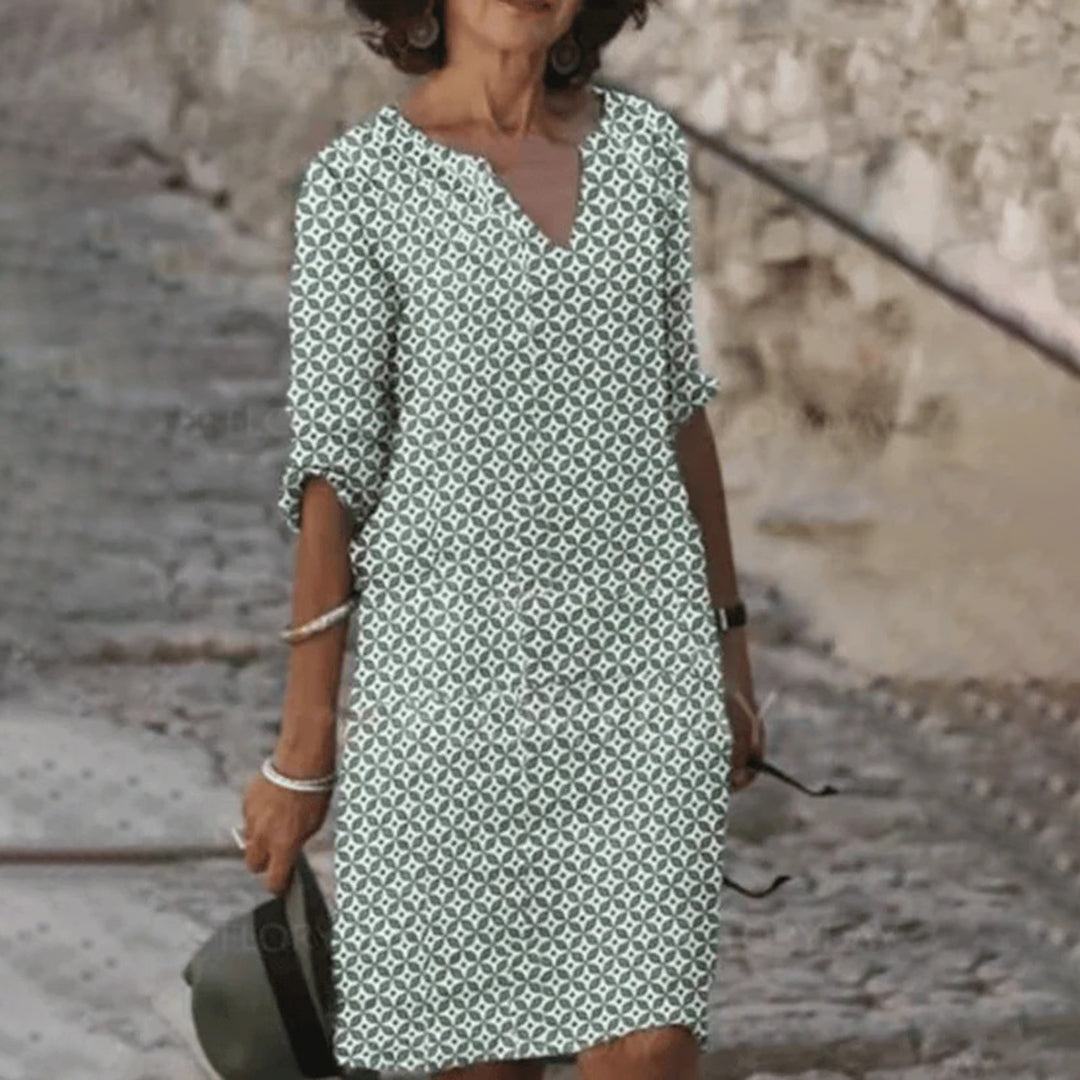 Vrouw in groene zomerjurk met geometrisch patroon, wandelend op een stenen pad. Stijlvolle damesmode, casual en elegant.