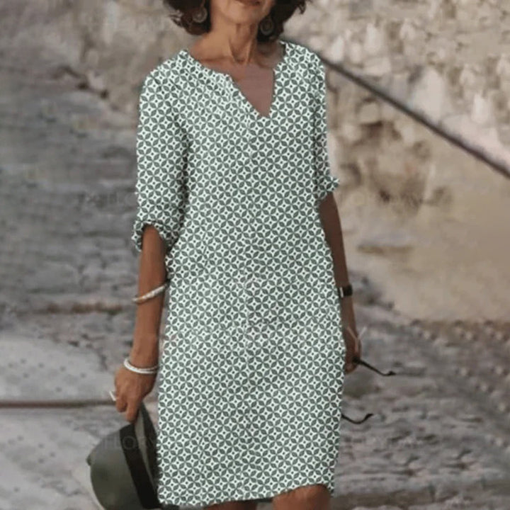 Vrouw in groene zomerjurk met geometrisch patroon, wandelend op een stenen pad. Stijlvolle damesmode, casual en elegant.