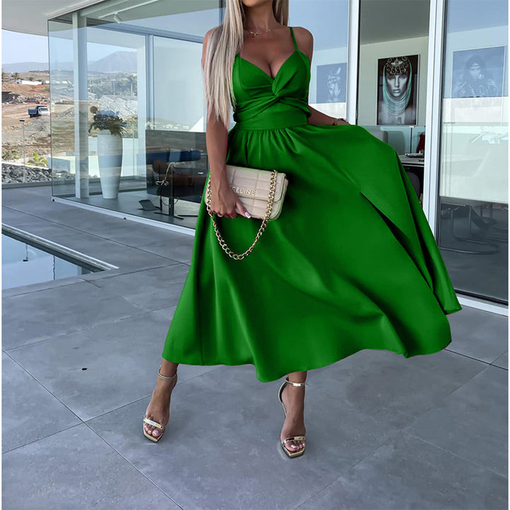 Vrouw in elegante groene jurk met gouden sandalen en beige handtas, staand op modern terras. Perfect voor zomerfeest of bruiloft.