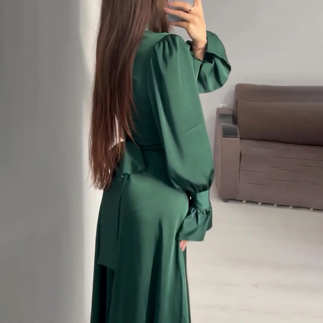 Vrouw in lange groene jurk met lange mouwen, staand in moderne woonkamer. Elegante damesmode, stijlvolle outfit, trendy kleding.