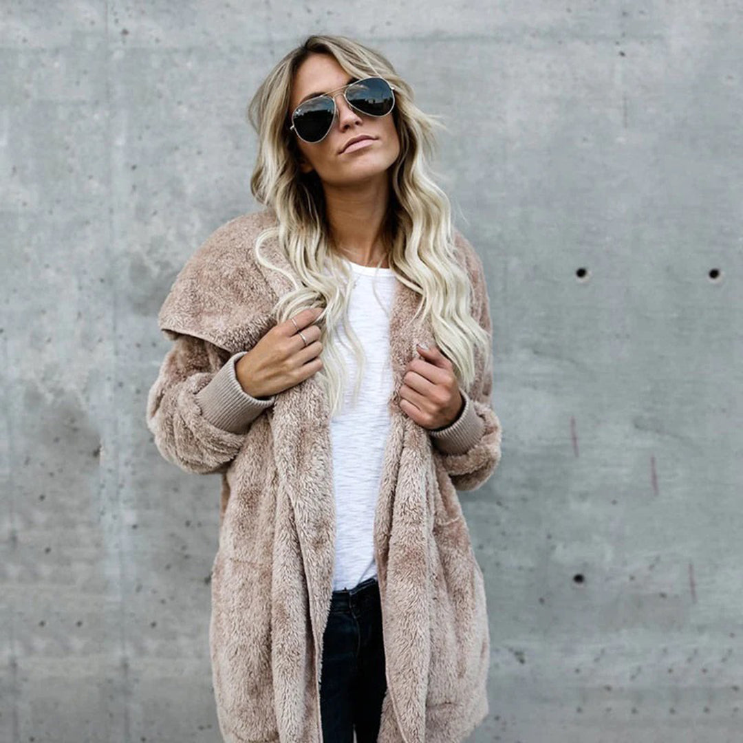 Vrouw in beige teddyjas en zonnebril tegen betonnen muur, modieuze winterkleding, trendy damesmode, casual stijl, lange blonde haren.