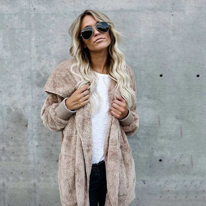 Vrouw in beige teddyjas en zonnebril tegen betonnen muur, modieuze winterkleding, trendy damesmode, casual stijl, lange blonde haren.