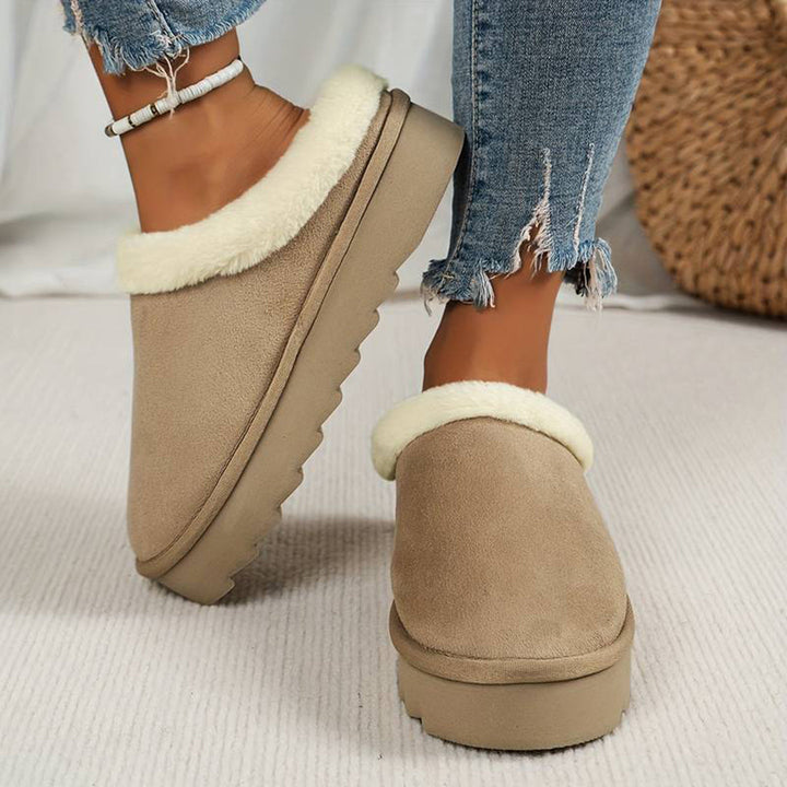 Khaki dames pantoffels met witte voering, gedragen met gescheurde jeans. Comfortabele winterse slippers, ideaal voor thuis.