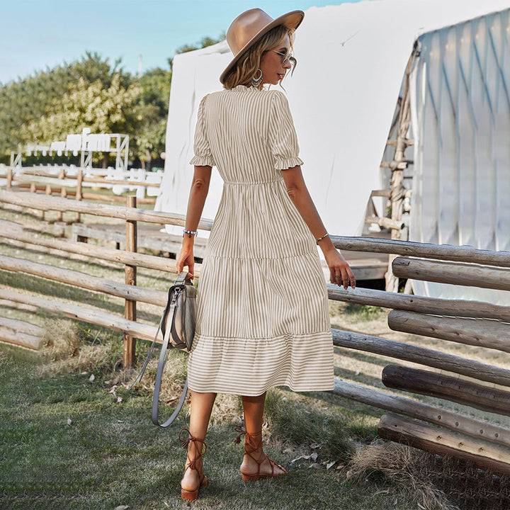 Vrouw in gestreepte khaki jurk en hoed, poseert buiten bij houten hek. Zomermode, casual stijl, dameskleding, bohemian look.
