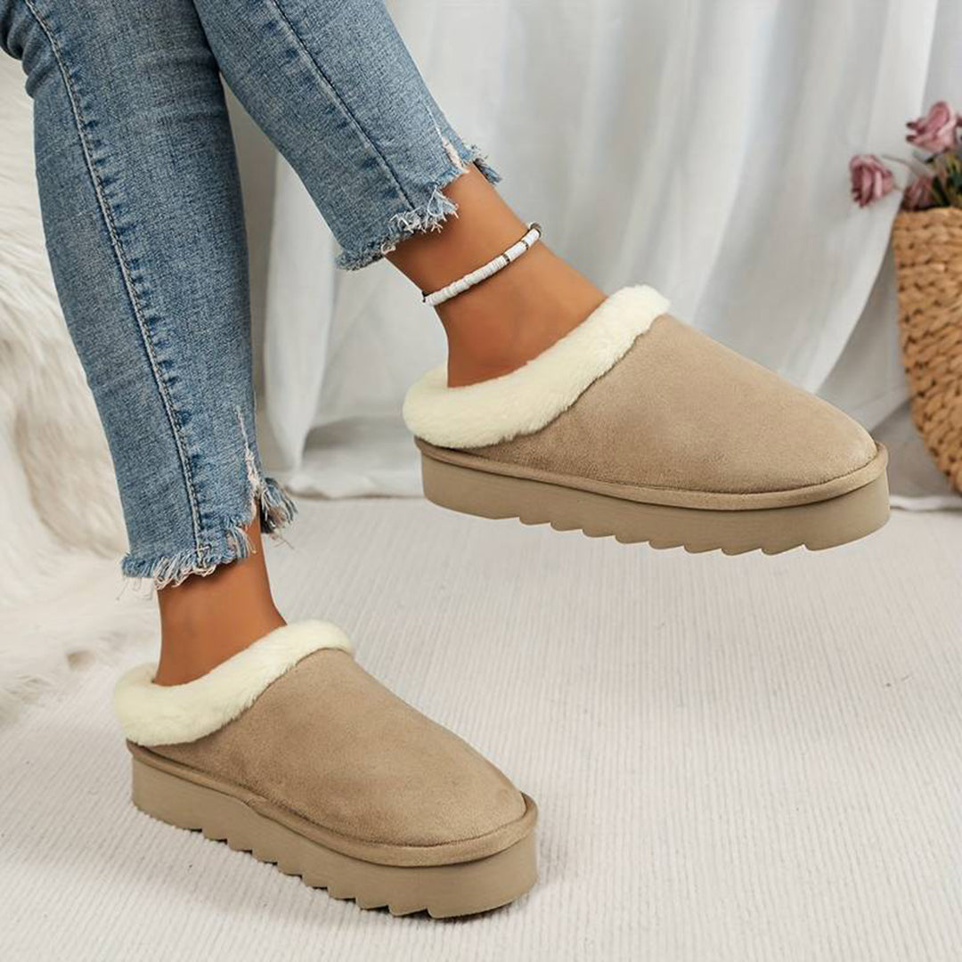 Vrouw draagt beige suède pantoffels met witte voering, gecombineerd met gescheurde jeans. Comfortabele wintermode, trendy damespantoffels.