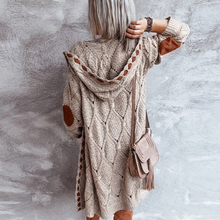 Vrouw in gebreide beige trui met capuchon en elleboogstukken, draagt een bruine schoudertas. Stijlvolle herfstmode, casual dameskleding.