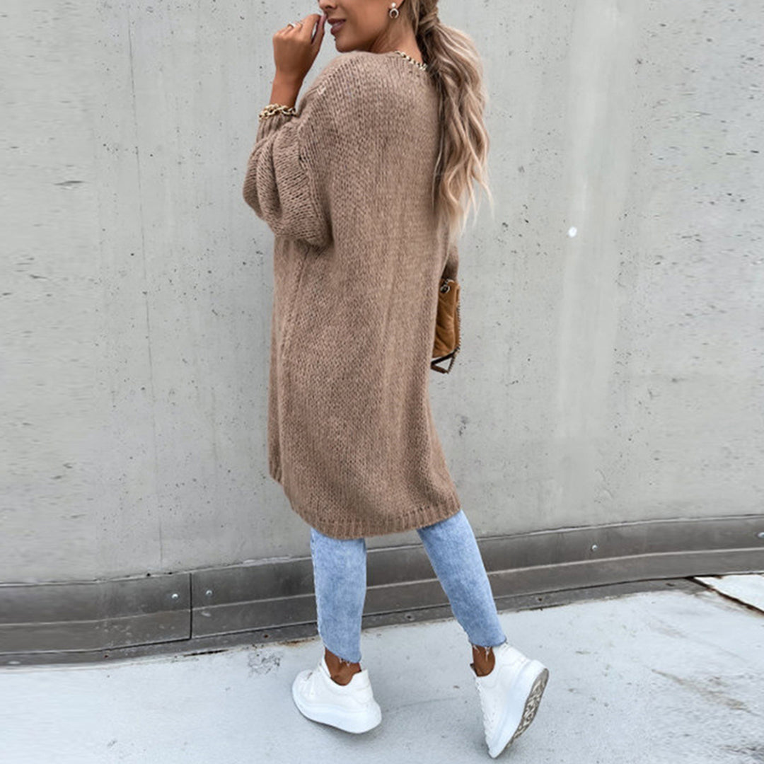 Vrouw in oversized khaki trui, blauwe jeans en witte sneakers, poseert tegen betonnen muur. Modieuze herfstoutfit, casual streetwear stijl.