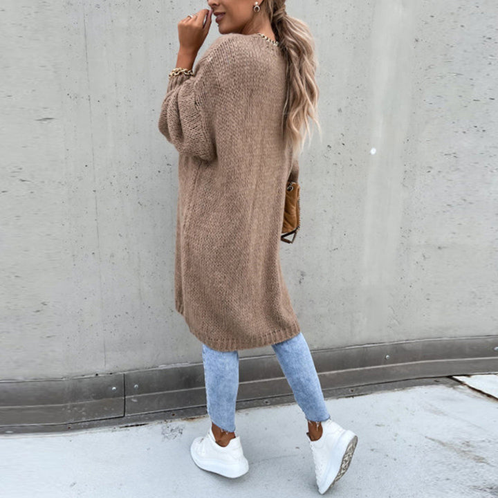 Vrouw in oversized khaki trui, blauwe jeans en witte sneakers, poseert tegen betonnen muur. Modieuze herfstoutfit, casual streetwear stijl.