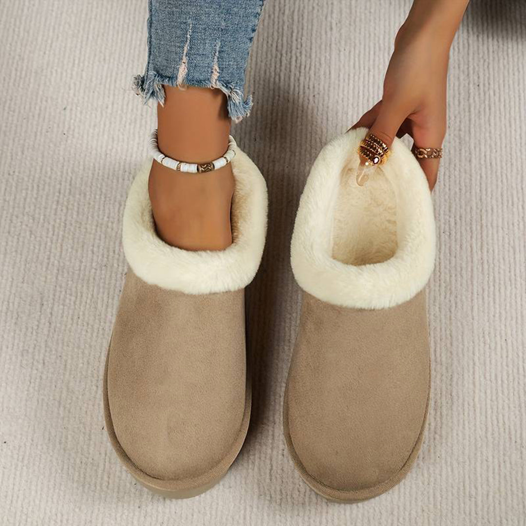 Khaki dames pantoffels met witte pluche voering, gedragen op een beige tapijt. Comfortabele winterse huisschoenen, ideaal voor koude dagen.