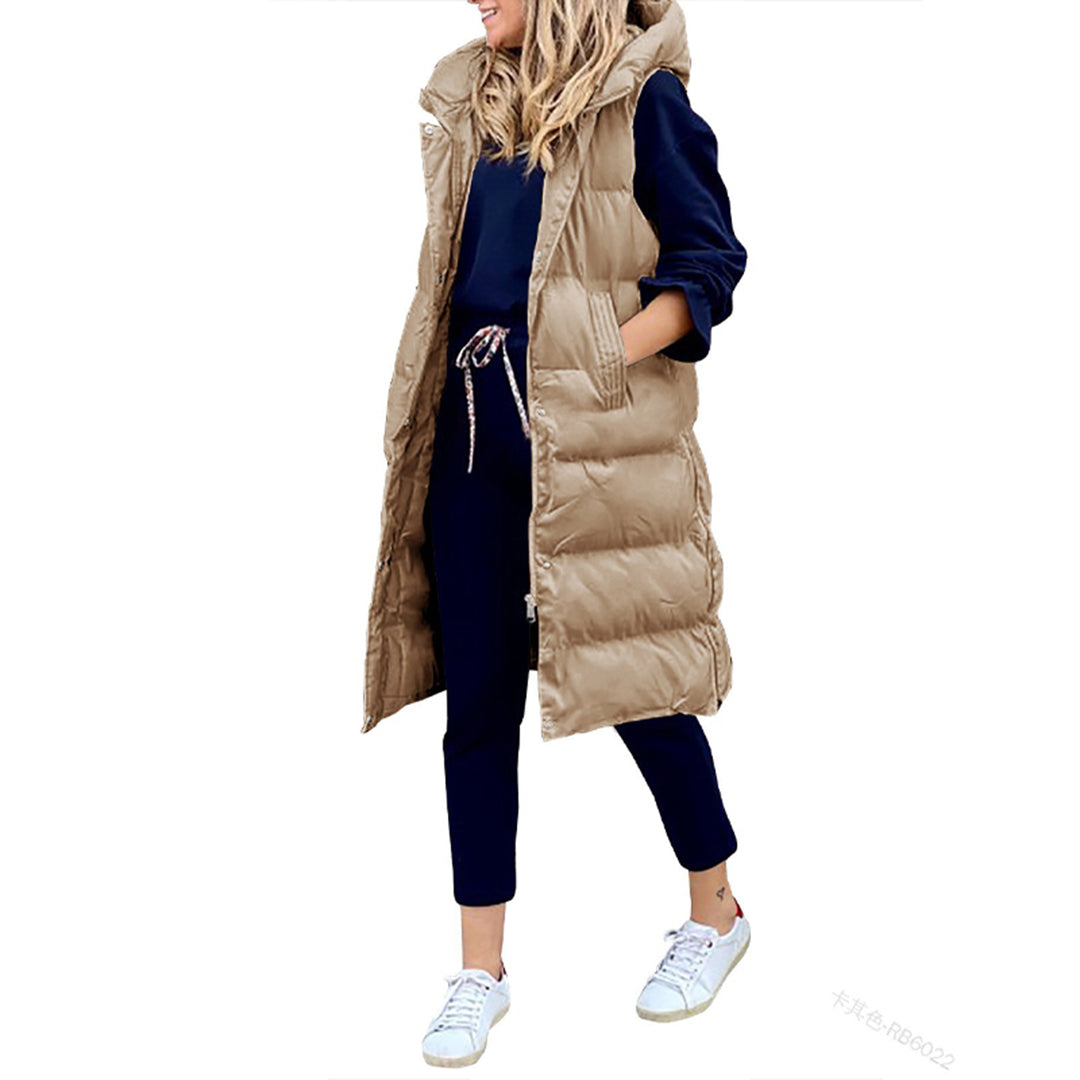 Damesmode: Lange khaki gewatteerde bodywarmer met capuchon, gedragen over een donkerblauwe outfit en witte sneakers. Stijlvolle herfstkleding.
