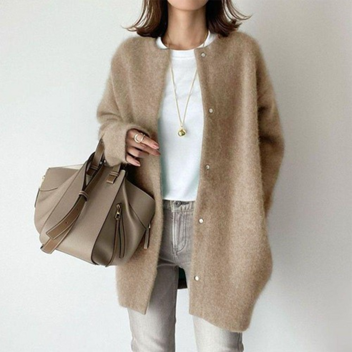 Vrouw draagt een beige wollen vest met knopen, witte top en grijze jeans, en houdt een stijlvolle khaki handtas vast. Modieuze dameskleding.