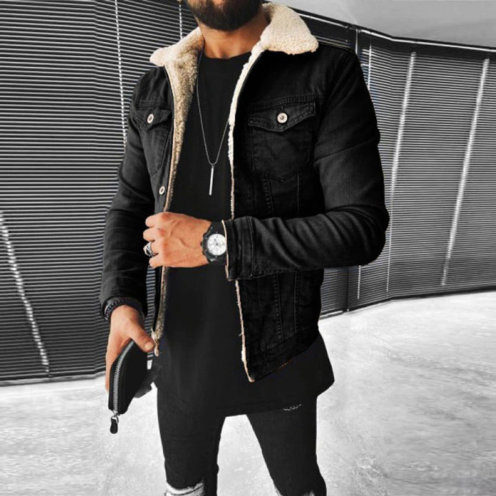 Man in zwarte spijkerjas met schapenvachtkraag, zwarte broek en horloge, houdt een portemonnee vast. Stijlvolle herenkleding, moderne mode.