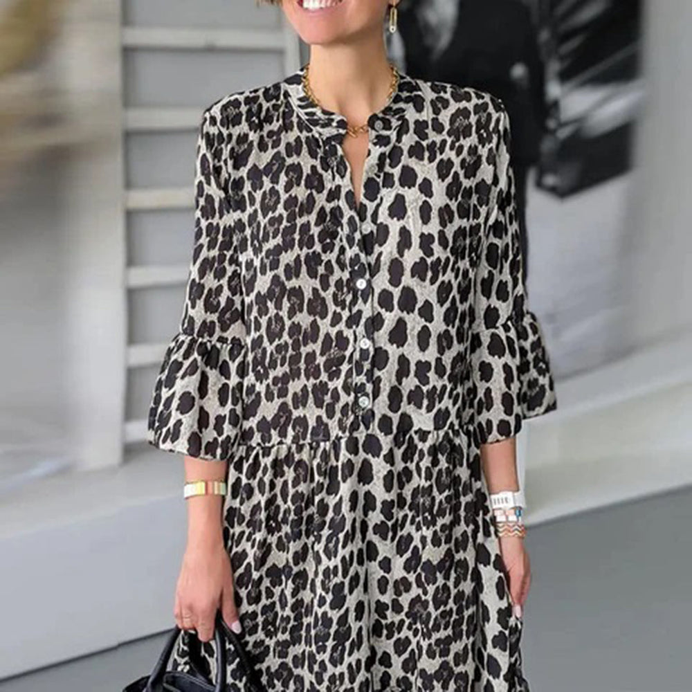 Vrouw in luipaardprint jurk met knopen, driekwart mouwen en ruches, draagt een zwarte tas. Modieuze dameskleding, trendy luipaardmotief.