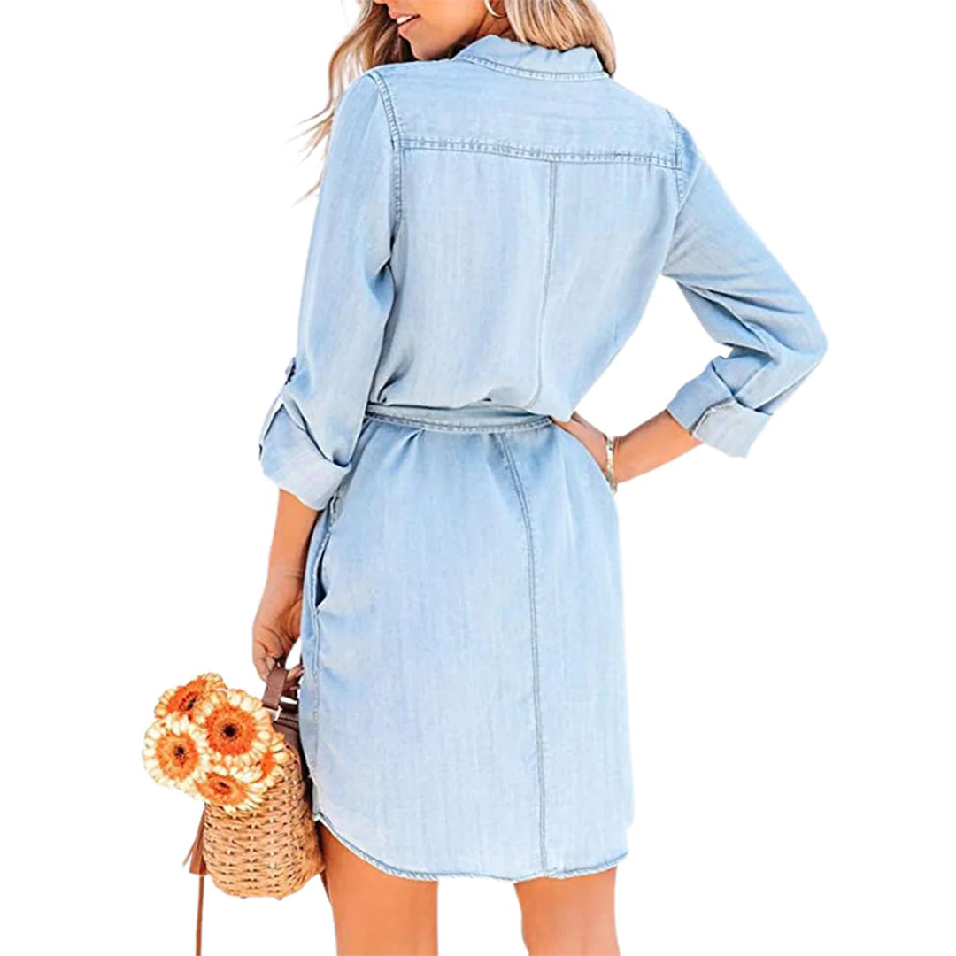 Vrouw in lichtblauwe denim jurk met lange mouwen, draagt een rieten tas met oranje bloemen. Casual mode, zomeroutfit, dameskleding.