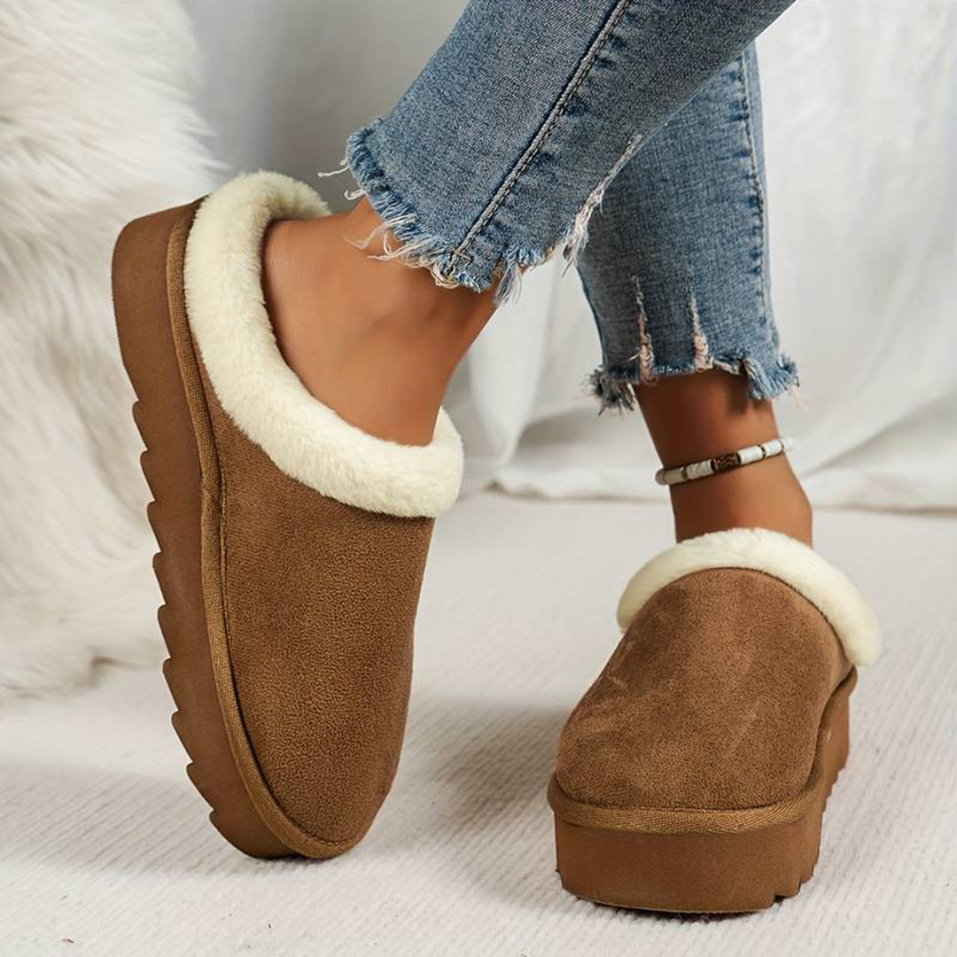Lichtbruine dames pantoffels met witte voering, gedragen met gescheurde jeans. Comfortabele winterse slippers, ideaal voor thuisgebruik.
