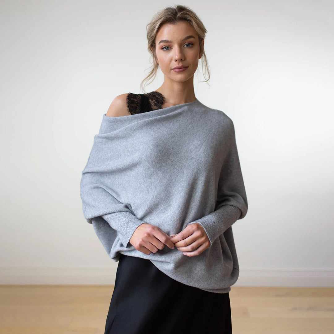 Vrouw draagt lichtgrijze oversized trui met blote schouder, gecombineerd met zwarte rok. Modieuze dameskleding, herfst-winter stijl.