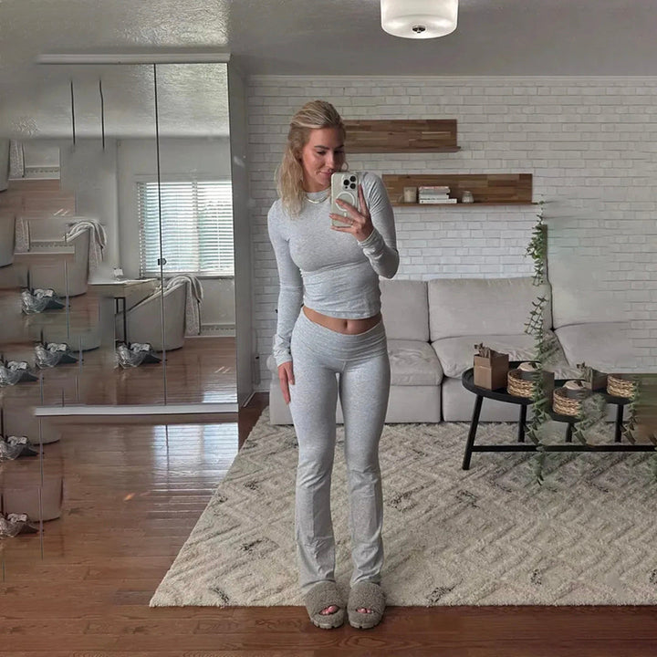 Vrouw in comfortabele grijze loungekleding poseert in moderne woonkamer met witte bank, houten vloer en decoratieve planten.