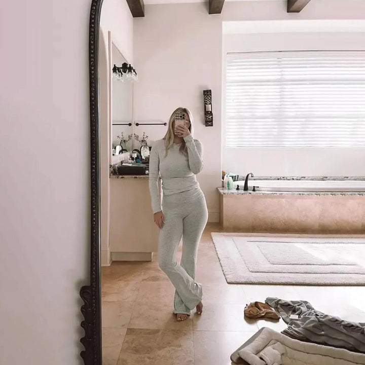 Vrouw in comfortabele grijze loungeset poseert voor een spiegel in een moderne badkamer. Luxe interieur, ontspanning, mode, thuiscomfort.