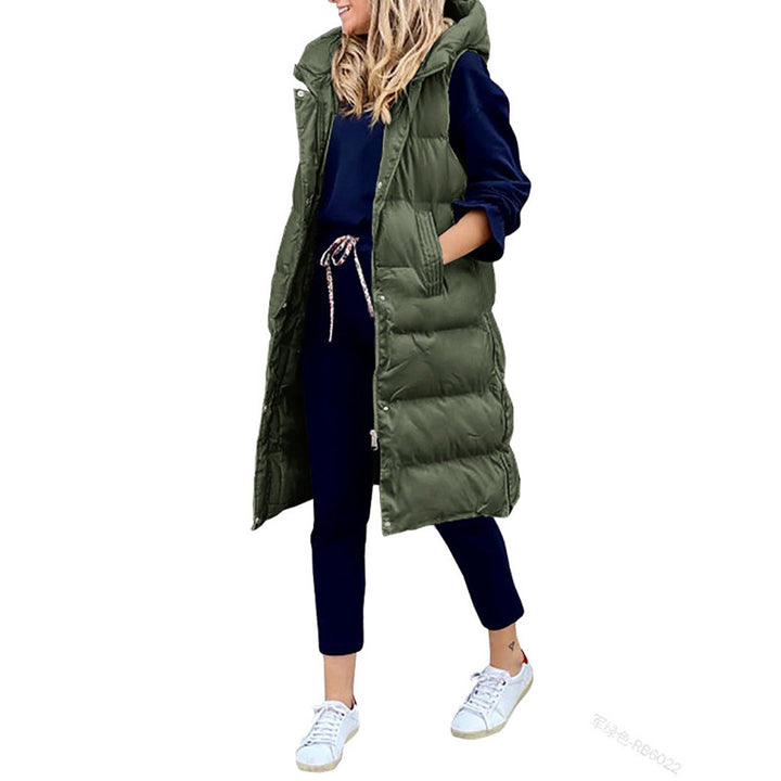 Vrouw in lange, militaire groene gewatteerde bodywarmer met capuchon, draagt donkerblauwe outfit en witte sneakers. Stijlvolle wintermode.