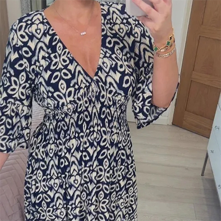 Vrouw in navy blauwe jurk met wit patroon, V-hals en driekwart mouwen, maakt selfie in slaapkamer. Trendy damesmode, casual zomerjurk.
